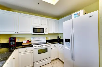 a kitchen with white cabinets and a white refrigerator at PCB Condo with Resort Amenities and Ocean Views in Panama City Beach