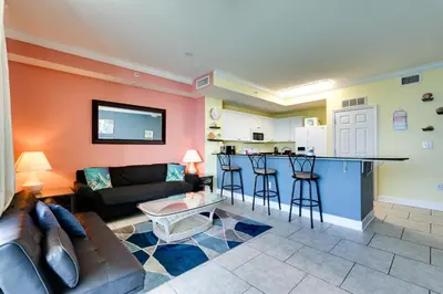 a living room with a couch and a kitchen at PCB Condo with Resort Amenities and Ocean Views in Panama City Beach