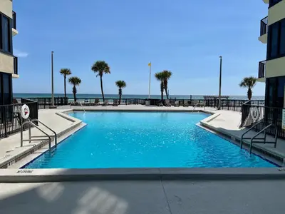a swimming pool with palm trees and the ocean in the background at 1st Floor Resort Condo! No Elevators! Free Beach Chair Service! by Dolce Vita Getaways PCB in Panama City Beach