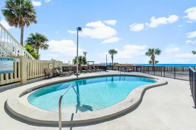 a swimming pool with palm trees and a fence at 1st Floor Resort Condo! No Elevators! Free Beach Chair Service! by Dolce Vita Getaways PCB in Panama City Beach