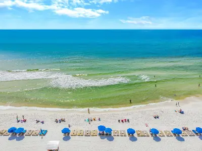 a beach with blue umbrellas and people on the beach at Grand Panama #1-1704 in Panama City Beach