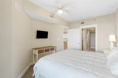 a white bedroom with a bed and a tv at Grand Panama #2-0505 in Panama City Beach