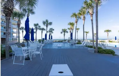 a patio with tables and chairs and palm trees at Dunes of Panama E605 2BR 2BA BEACHFRONT condo in Panama City Beach