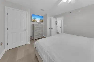 a white bedroom with a white bed and a dresser at Sterling Beach #406 in Panama City Beach