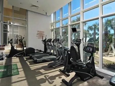 a gym with treadmills and ellipticals in a room with windows at Sterling Beach #406 in Panama City Beach