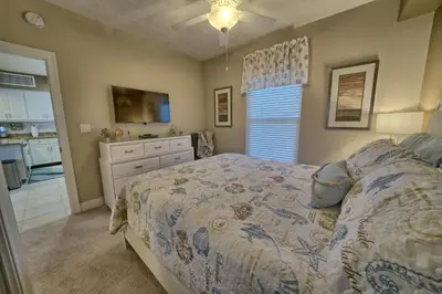 a bedroom with a bed with a dresser and a kitchen at Oceanfront Paradise with Pool Access - 0606 condo in Panama City Beach