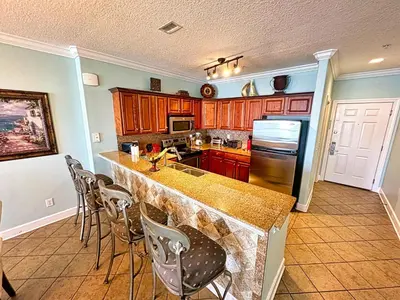 a kitchen with wooden cabinets and a counter with chairs at Tropic Winds 701 in Panama City Beach