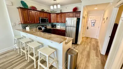 a kitchen with a counter with stools and a refrigerator at Tropic Winds 2305 in Panama City Beach