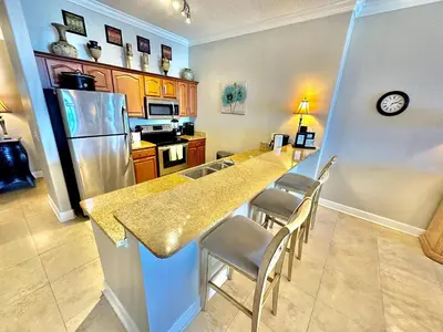 a kitchen with a counter with chairs and a refrigerator at Ocean Reef 2001 in Panama City Beach