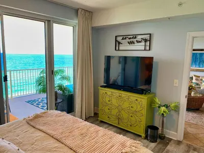 a bedroom with a television and a balcony with the ocean at Ocean Reef 1403 in Panama City Beach