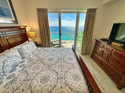 a bedroom with a bed and a television and a balcony at Ocean Reef 2303 in Panama City Beach