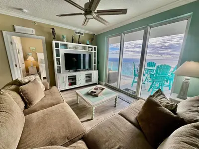 a living room with a couch and a tv and a balcony at Tropic Winds 2209 in Panama City Beach