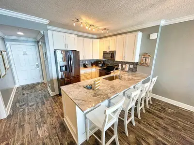 a kitchen with a large island with white chairs at Tropic Winds 1604 in Panama City Beach