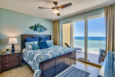 a bedroom with a bed and a balcony with the ocean at Tropic Winds 703 in Panama City Beach