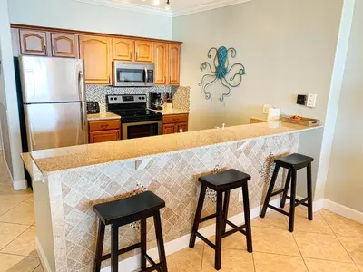 a kitchen with a counter with two stools and a refrigerator at Ocean Reef 1604 in Panama City Beach
