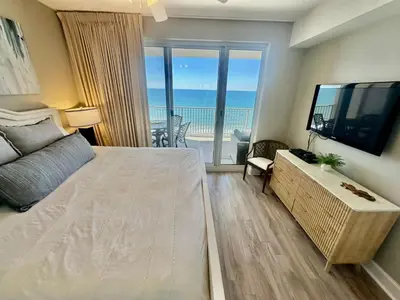 a bedroom with a bed and a television and a balcony at Ocean Reef 1107 in Panama City Beach