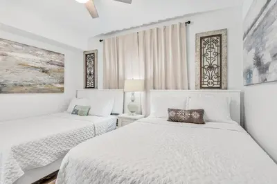 two beds in a white bedroom with white walls at Tropic Winds 1909 in Panama City Beach
