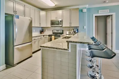 a kitchen with white cabinets and a bar with stools at Tropic Winds 707 in Panama City Beach