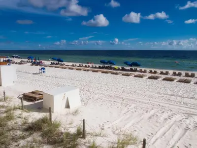 a beach with chairs and umbrellas and the ocean at Tropic Winds 707 in Panama City Beach