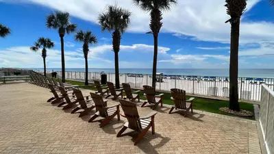 a row of wooden chairs and palm trees next to the beach at Tropic Winds 1107 in Panama City Beach