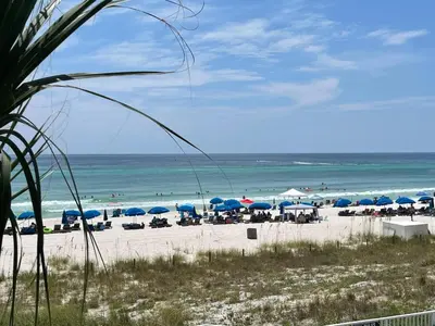 a beach with blue umbrellas and chairs and the ocean at Ocean Reef 2204 in Panama City Beach
