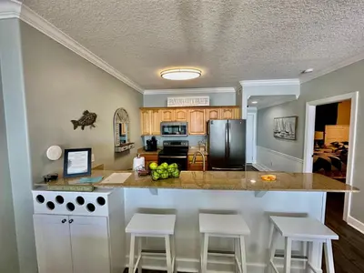 a kitchen with a counter with stools and a refrigerator at Ocean Reef 1705 in Panama City Beach