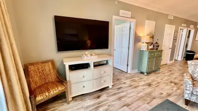 a living room with a flat screen tv and a chair at Tropic Winds 904 in Panama City Beach