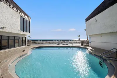 a large swimming pool next to a building with the ocean at Beach Haven! 2BR 2BA Sleeps 6! Coastal paradise awaits! in Panama City Beach