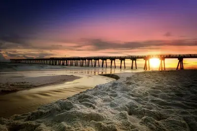 a pier on a beach with the sun setting at Sand Castle in Panama City Beach