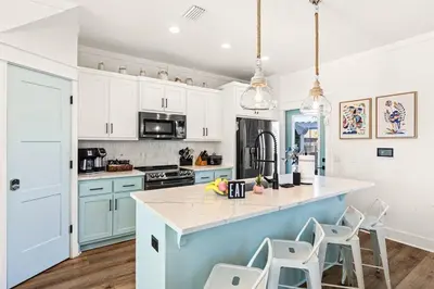 a kitchen with white cabinets and a blue island with stools at Sand Castle in Panama City Beach