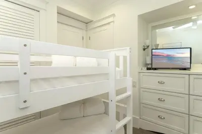 a white bedroom with a bunk bed and a tv at Barefoot at the Beach in Watersound Beach