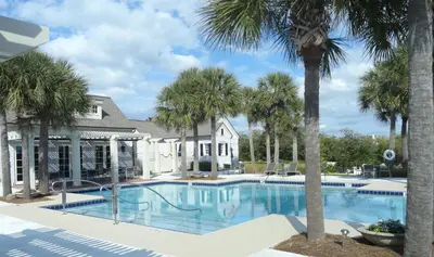 a swimming pool with palm trees in front of a house at The Golden Pearl in Watersound Beach