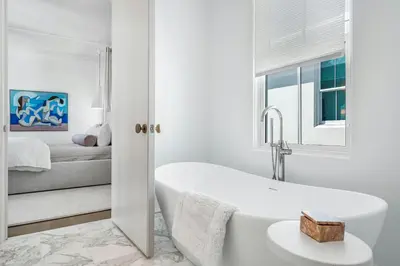 a white bathroom with a tub and a bedroom at 30A Showhouse in Rosemary Beach