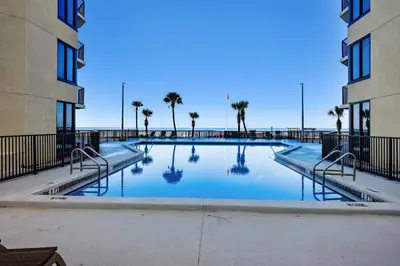 a swimming pool between two buildings with palm trees at Sunbird 102E By Book That Condo in Panama City Beach