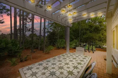 an outdoor patio with a white table and chairs at Treasure Palms - Golf Cart- Bikes - Arcade- Peloton- Near Rosemary - Community Pool in Rosemary Beach