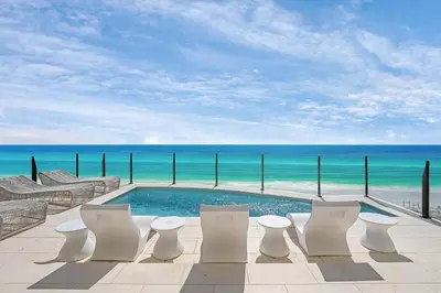 a swimming pool with white chairs and the ocean at Costa Fortune in Inlet Beach