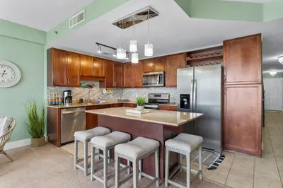 a kitchen with wooden cabinets and a large island with bar stools at Nautical Nest at Laketown Wharf #1019 by Nautical Properties in Panama City Beach