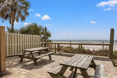 a picnic table and benches on a patio near the beach at Grandview Oasis! 3BR 2BA Sleeps 9! Gulf-front tranquility beckons! in Panama City Beach