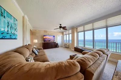 a large living room with a large couch and large windows at Palmetto Beachfront Hotel, a By The Sea Resort in Panama City Beach