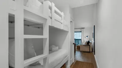 a bedroom with white bunk beds and a living room at Beachside Condo 24 Here comes the Sun in Santa Rosa Beach