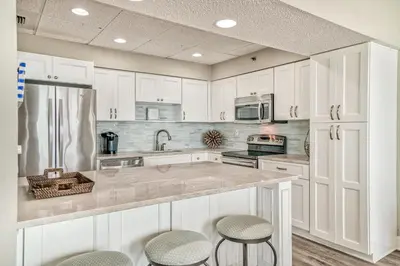 a kitchen with white cabinets and a counter with stools at HP 36W Condo by 30A Escapes in Rosemary Beach