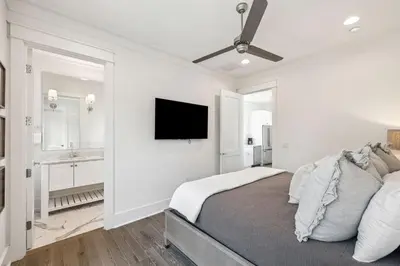 a white bedroom with a bed and a flat screen tv at Tidey Whitey by 30A Escapes in Seacrest