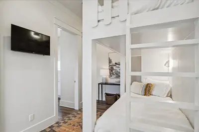 a white bedroom with a bunk bed with a flat screen tv at Sea Ya Soon by 30A Escapes in Rosemary Beach