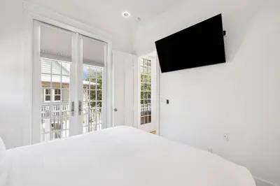 a white bedroom with a bed and a flat screen tv at Tuscan Blue by 30A Escapes in Rosemary Beach