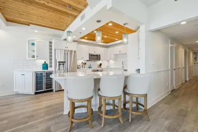 a kitchen with white cabinets and a large island with bar stools at HP 21W Gulf Front Condo by 30A Escapes in Rosemary Beach