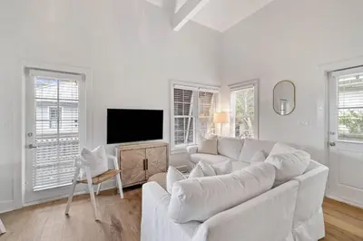 a white living room with a white couch and a tv at Stairway to Heaven Carriage by 30A Escapes in Rosemary Beach