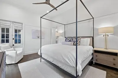 a white bedroom with a canopy bed and a chair at Stairway to Heaven Cottage by 30A Escapes in Rosemary Beach