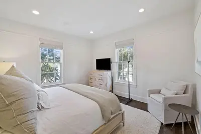 a white bedroom with a bed and a chair at Stairway to Heaven Cottage by 30A Escapes in Rosemary Beach