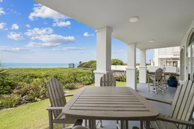 a wooden table and chairs on a porch with the ocean at Sunset Beach 102C by 30A Escapes in Rosemary Beach