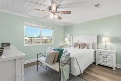 a bedroom with a bed with a ceiling fan and a chair at Searenity Now by 30A Escapes in Seagrove Beach